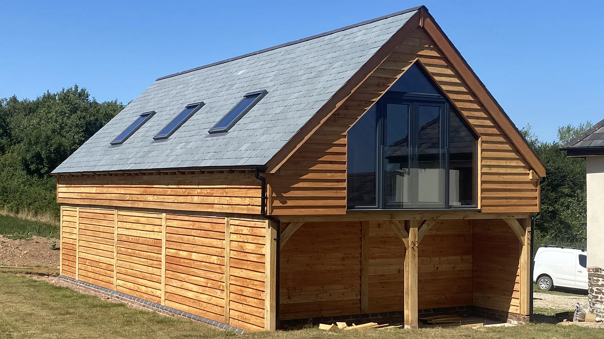 Two-storey oak framed garage with cedar cladding, a slate roof and a glazed gable