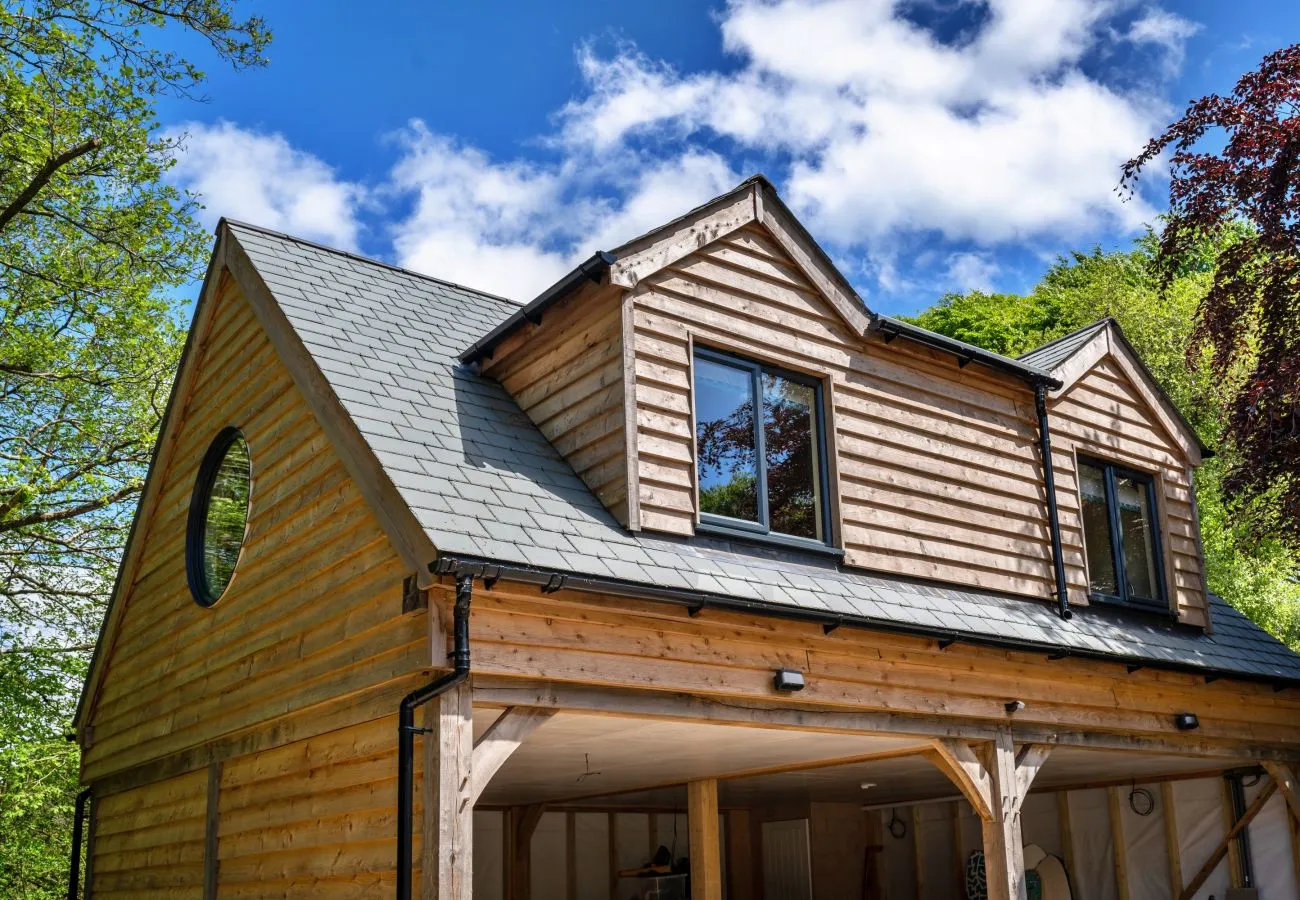 Cedar clad gable with a circular window and slate roof over an open oak bay