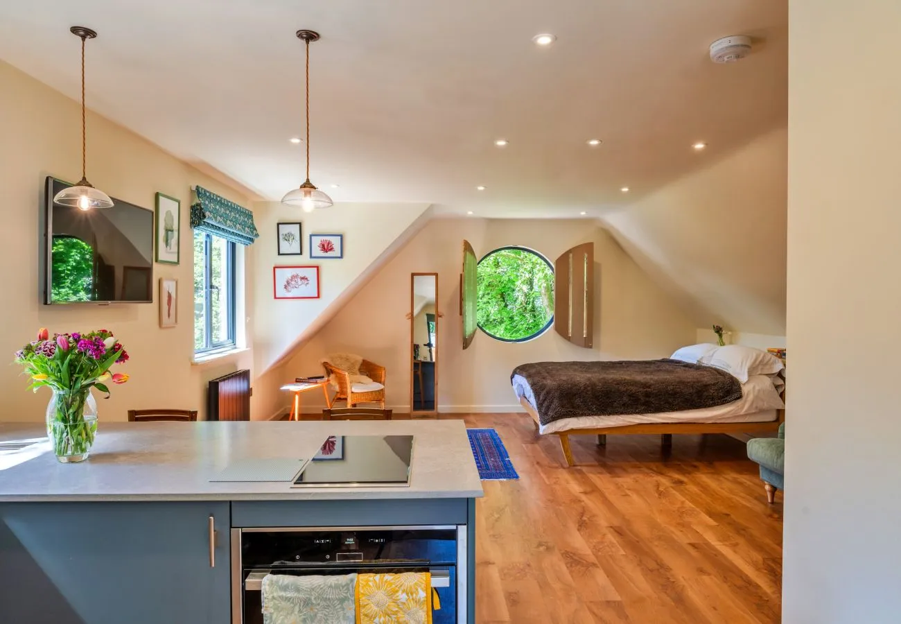 Open plan studio interior with kitchen, sitting area and bed under a vaulted ceiling