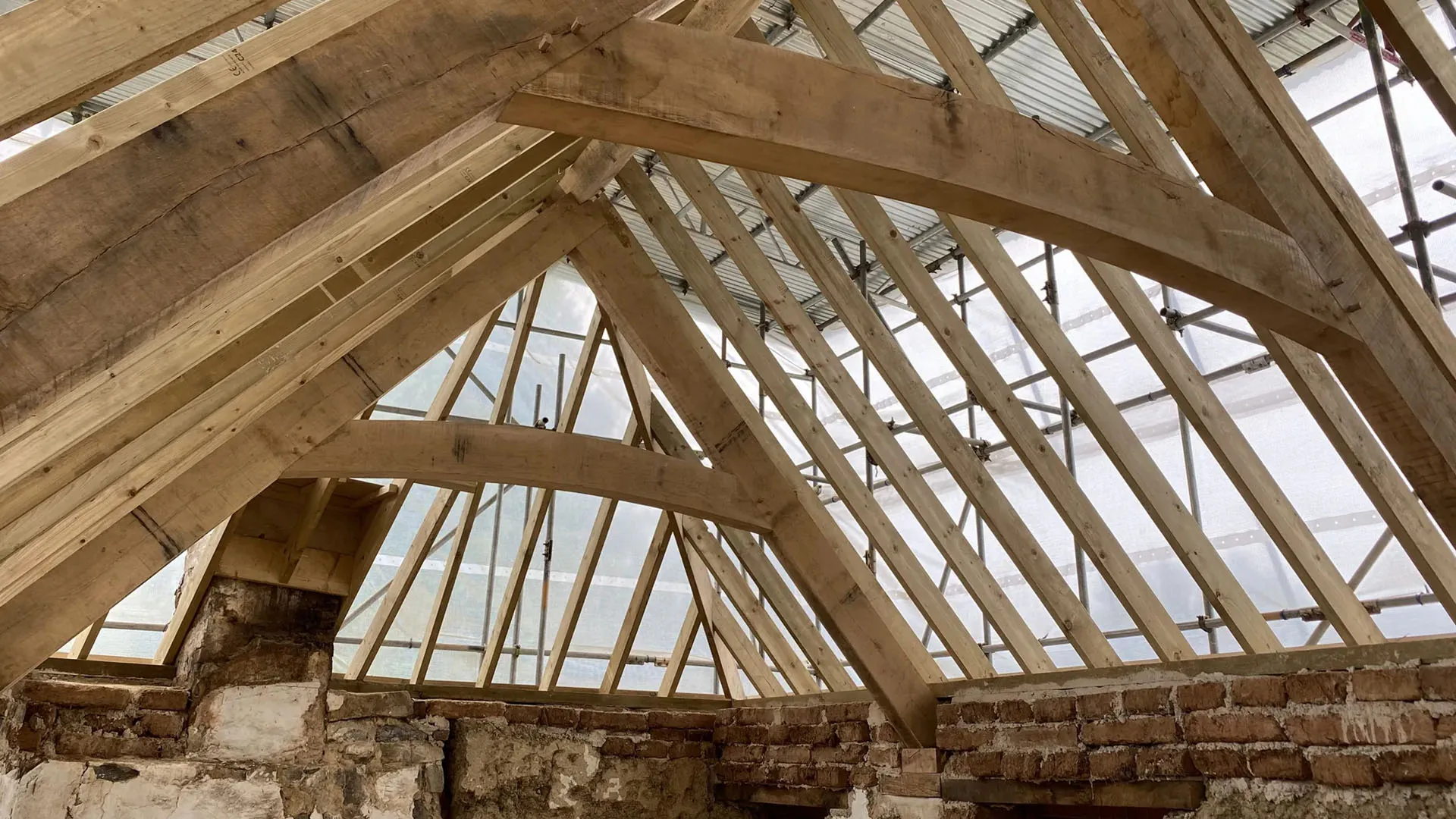 New oak roof trusses raised inside a stone barn under restoration